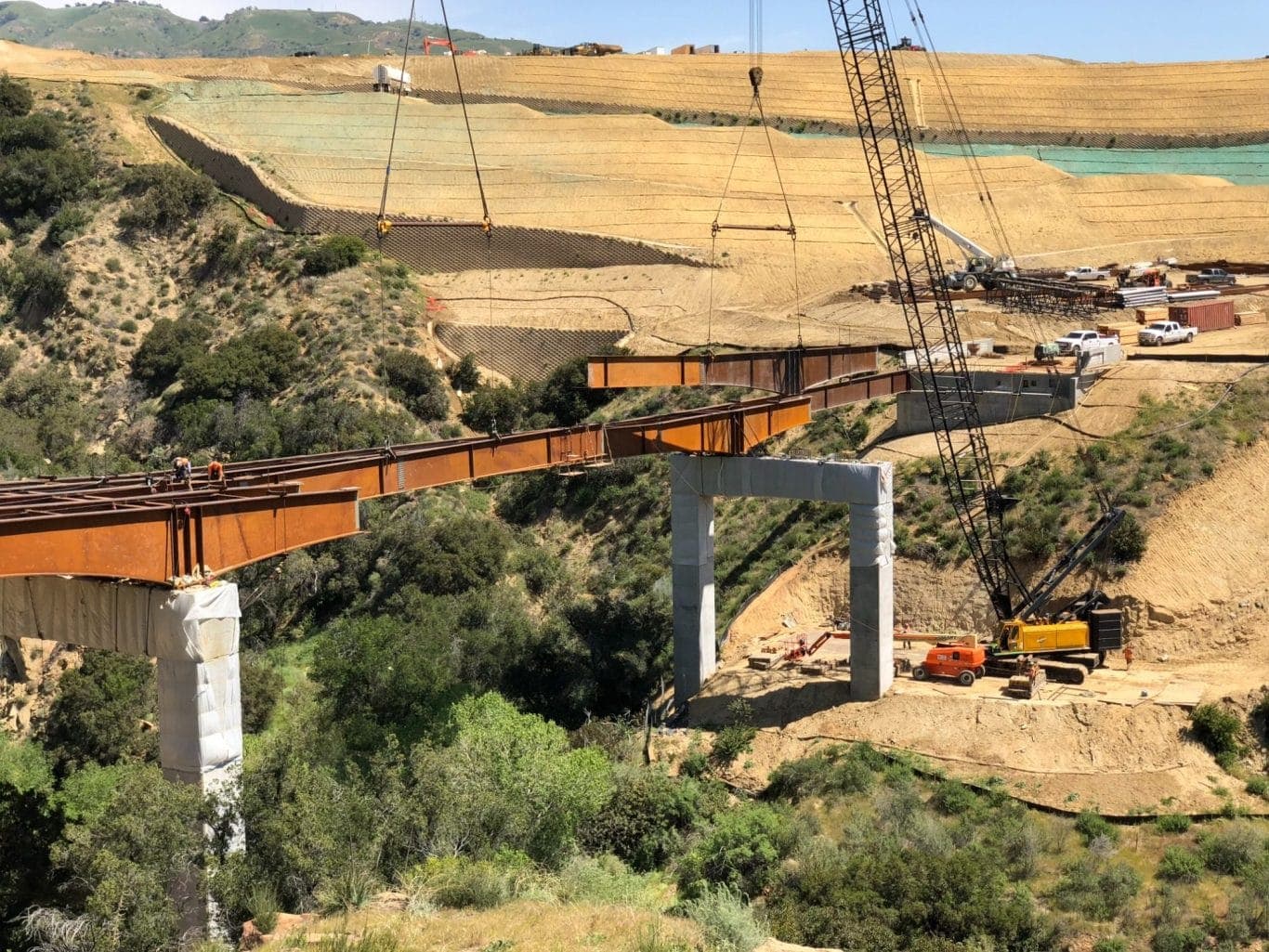 Steel bridge girders being set across a canyon during land development construction